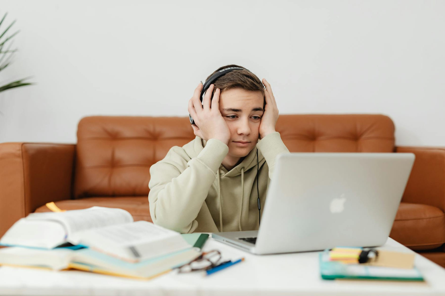 A young student wearing headphones, looking tired while studying with a laptop and books. on The Course Compass