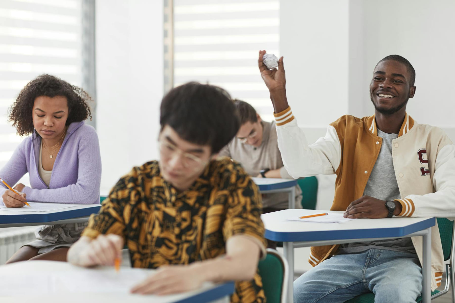 Students taking an exam in a diverse classroom, showing a mix of focus and playful interactions. on The Course Compass