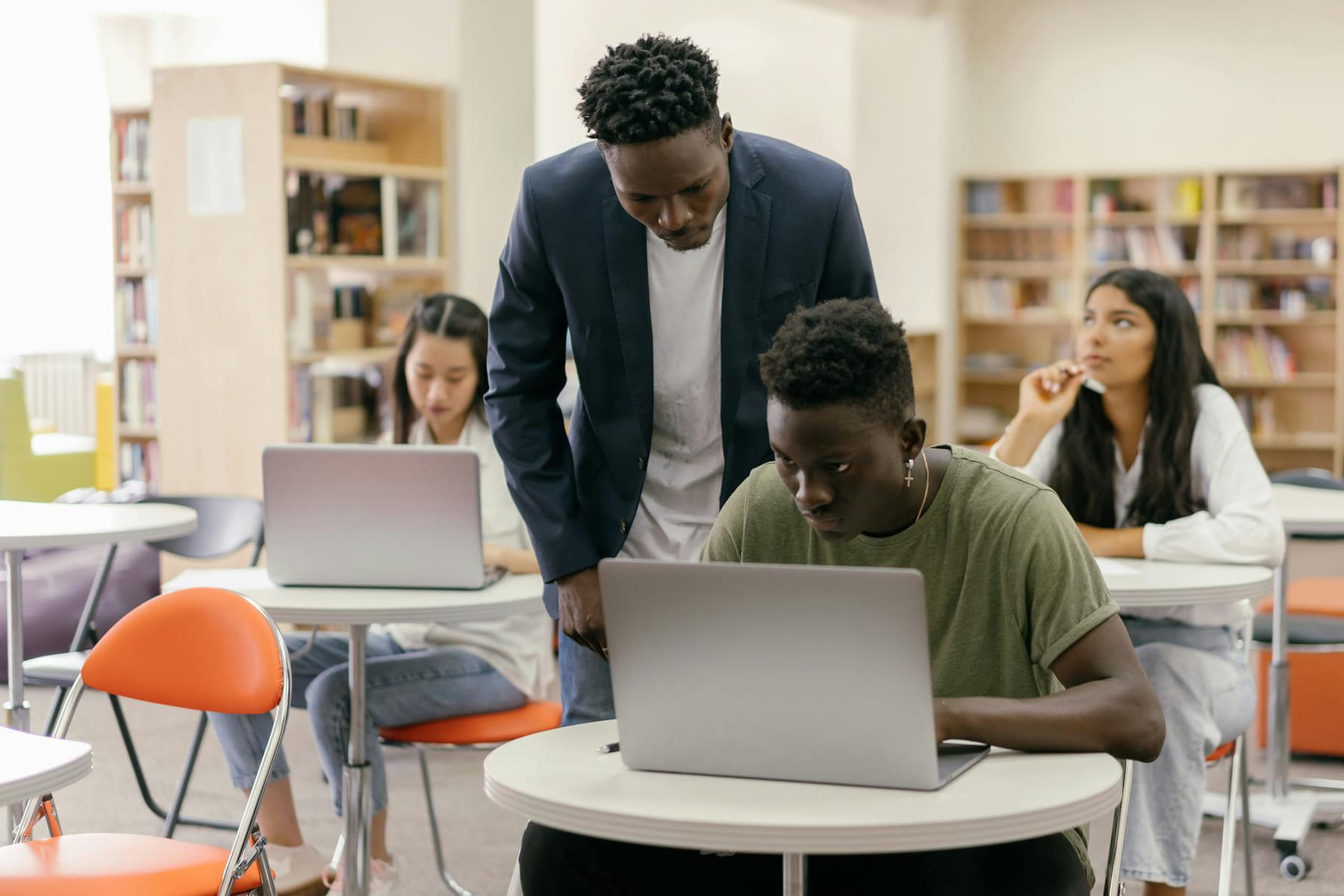 Students learning in a classroom setting with a teacher assisting and laptops on desks, creating an interactive education environment. on The Course Compass
