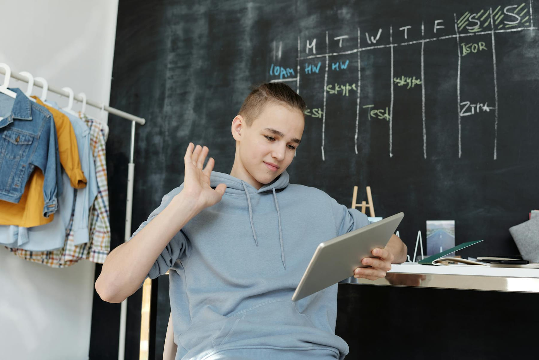 A teenager uses a tablet for online learning in a cozy home setting, waving at the screen. on The Course Compass