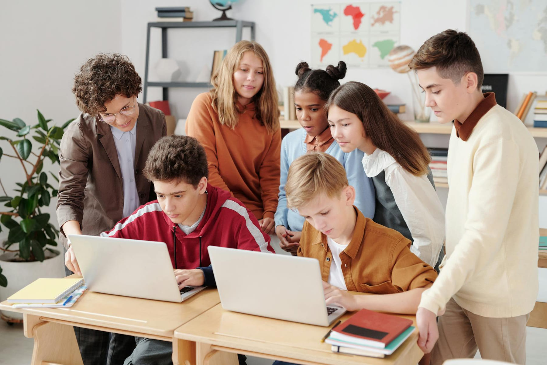 A group of diverse students collaborating on laptops in a classroom setting, guided by a teacher. on The Course Compass